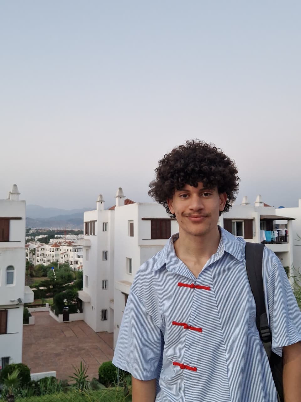 Adil Asselman, smiling, with white buildings and hills behind him at dusk